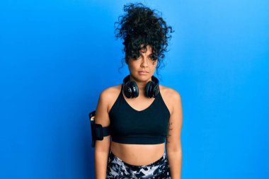 Spor kıyafetleri giyen, kulaklık takan, kuşkucu ve gergin genç İspanyol kadın sorun yüzünden surat asıyor. negatif kişi. 