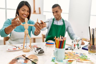 Genç Latin ressam çift mutlu bir şekilde gülümsüyor. Sanat stüdyosundaki masada manikin kullanıyor.