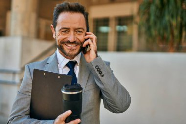 Orta yaşlı işadamı akıllı telefondan konuşuyor ve şehirde kahve içiyor..