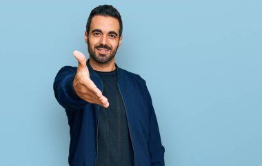 Gündelik kıyafetler giyen genç İspanyol adam dostça bir selamlama ve hoş geldin hediyesi olarak el sıkışmayı sunuyor. başarılı iş. 