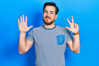 Sakallı, sıradan çizgili tişört giyen yakışıklı beyaz adam sekiz numarayı gösterip, gülümseyerek kendinden emin ve mutlu görünüyor.. 