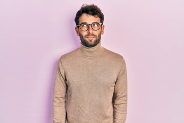 Balıkçı yaka kazak giyen ve gözlüklü yakışıklı bir adam gülümseyip yan tarafa bakıyor ve düşünüyor.. 