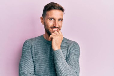 Sakallı, sıradan bir süveter giyen, kameraya kollarını kavuşturup çenesine dokunarak gülümseyen yakışıklı bir adam. Olumlu düşünmek. 