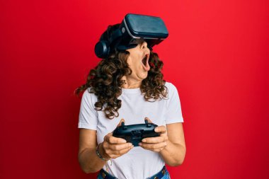 Sanal gerçeklik gözlüğü takan orta yaşlı bir kadın 3 boyutlu video oyunları oynuyor, gelecekteki simülasyonları izliyor, heyecan verici deneyimler yaşıyor.