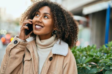 Genç Afrikalı Amerikalı kadın gülümsüyor. Şehirdeki akıllı telefondan mutlu bir şekilde konuşuyor..