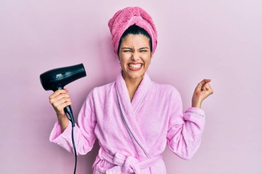 Genç İspanyol kadın duş bornozu giyiyor kurutucu kullanıyor gururla bağırıyor, zaferi kutluyor ve başarıyı kollarını kaldırarak kutluyor. 