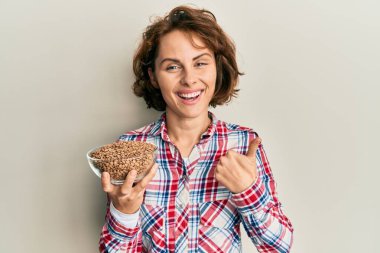 Genç esmer kadın elinde mercimeği fırına veriyor mutlu ve pozitif gülümsüyor, başparmağıyla mükemmel ve onay işareti yapıyor. 