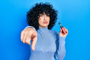 Orta Doğulu genç bir kadın elinde elektronik sigarayla kamerayı işaret ediyor ve sen kendine güvenen ciddi bir hareket yapıyorsun. 