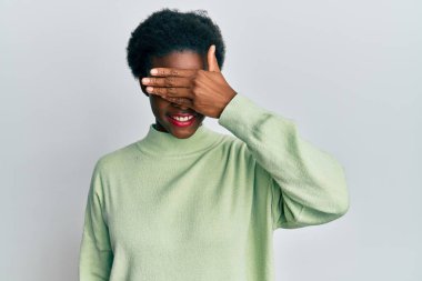 Gündelik kıyafetler giyen, gülümseyen ve gülen genç Afro-Amerikan kızı şaşırtmak için gözlerini kapatıyor. kör kavram. 