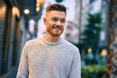 Genç beyaz adam gülümseyerek şehirde mutlu mesut duruyor..