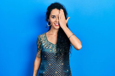 Bindi ve geleneksel kurta elbisesi giyen genç bir kadın bir gözünü eliyle kapatıyor, yüzünde kendine güvenen bir gülümseme ve şaşırtıcı bir duygu var.. 