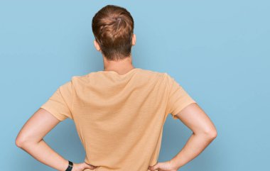 Gündelik giysiler giymiş, kolları vücudunda geriye doğru bakan genç beyaz bir adam. 