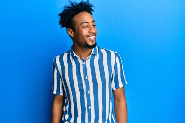 Sakallı, sıradan çizgili tişörtlü, yüzünde gülümseme, doğal bir ifade olan Afro-Amerikalı genç bir adam. Kendinden emin gülen. 