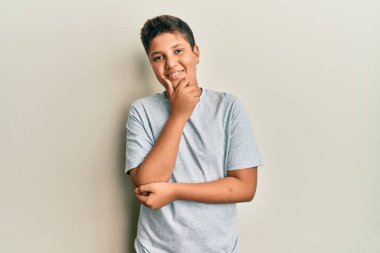 Gündelik gri tişört giyen genç İspanyol çocuk kameraya kendinden emin bakıyor kolları çapraz ve çenesi açık gülümsüyor. Olumlu düşünmek. 