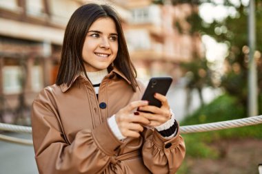 Genç, güzel esmer kadın dışarıda mutlu bir şekilde gülümsüyor akıllı telefon kullanıyor.