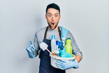 Genç İspanyol adam temizlik ürünlerini elinde tutuyor. Korkmuş ve ağzı açık kalmış, şaşırmış ve şaşırmış. 