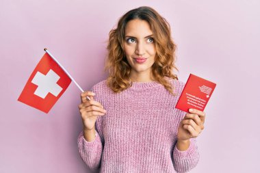 Elinde İsviçre bayrağı ve pasaportu olan beyaz bir kadın gülümsüyor ve yan tarafa bakıyor.. 