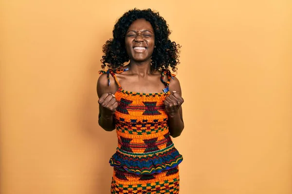 アフリカの伝統的な服を着た若いアフリカ系アメリカ人女性が腕を上げて成功に興奮し 勝利を笑顔で祝う目を閉じた 勝者のコンセプト — ストック写真