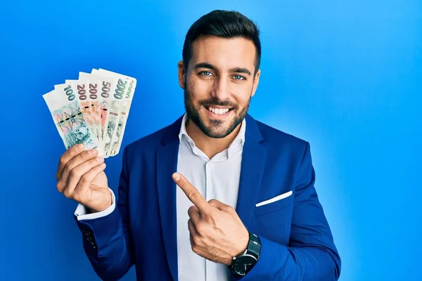 若いヒスパニック系のビジネスマンは ビジネススーツを着て手と指で幸せなポインティングを笑顔Czechコルナ紙幣を保持 — ストック写真