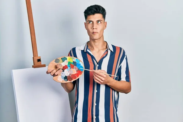 Young Hispanic Man Holding Painter Palette Paintbrush Standing Close Canvas — Photo