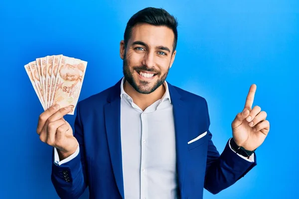 脇に手や指で笑顔幸せなポインティングトルコのリラの紙幣を保持ビジネススーツを身に着けている若いヒスパニック系のビジネスマン — ストック写真