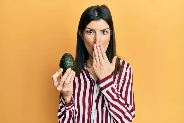 Ung Latinamerikansk Kvinna Håller Avokado Täcker Munnen Med Handen Chockad — Stockfoto