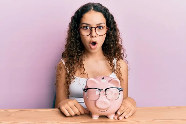 Tiener Hispanic Meisje Holding Piggy Bank Met Bril Bang Verbaasd — Stockfoto