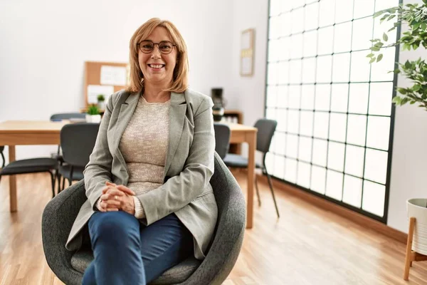 Middle age businesswoman smiling happy sitting with arms crossed gesture at the office.