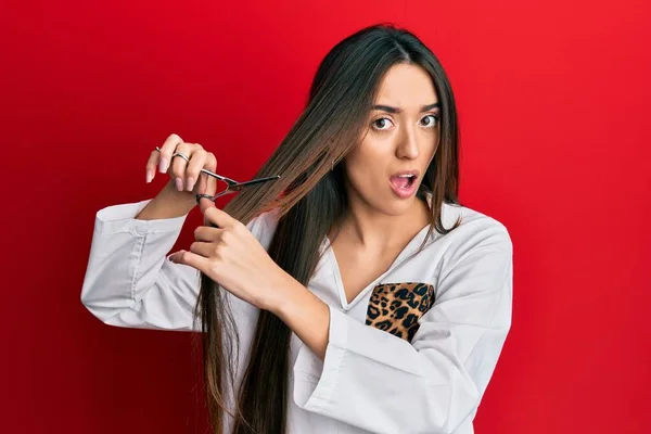 Young Hispanic Girl Cutting Hair Using Scissors Shock Face Looking — Stock Photo, Image
