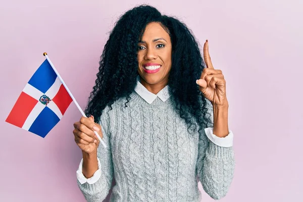 中世アフリカ系アメリカ人女性ドミニカ共和国の旗を持つ幸せな顔をしたアイデアや質問を指差す指で笑顔 ナンバーワン — ストック写真