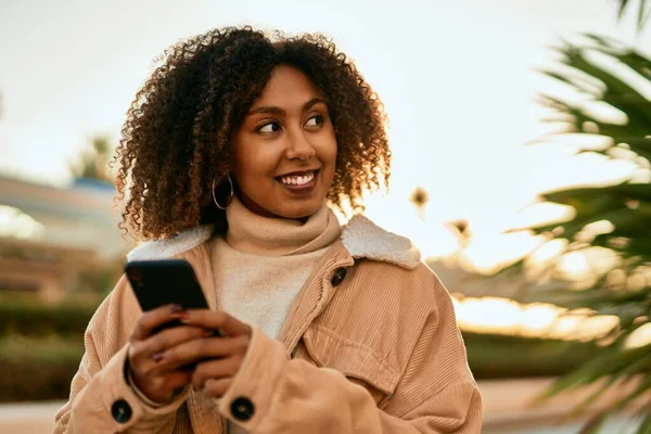 若いアフリカ系アメリカ人の女性が市内のスマートフォンを使って笑顔で — ストック写真