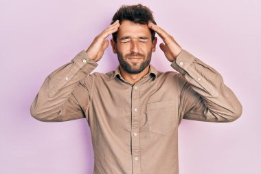 Sakallı, sıradan tişörtlü, eli başının üstünde yakışıklı bir adam. Stres yüzünden başı ağrıyor. migren ağrısı. 