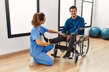 Genç engelli adam klinikte tekerlekli sandalyede oturarak hareket egzersizi yapıyor..