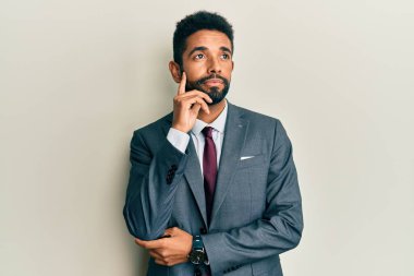 Sakallı, takım elbiseli ve eli çenesinde kravatlı yakışıklı İspanyol bir adam soru sormayı düşünüyor, düşünceli bir ifade. Gülümseyen ve düşünceli bir yüz. şüphe kavramı. 