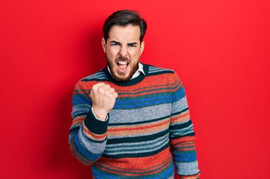 Sakallı, zarif yün kazak giyen yakışıklı beyaz adam öfkeyle bağırırken kızgın ve kızgın yumruk kaldırıyor. öfke ve agresif konsept. 