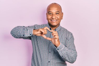 Orta yaşlı, sıradan kıyafetler giyen, aşık gülümseyen, elleriyle kalp sembolü yapan Latin bir adam. romantik kavram. 