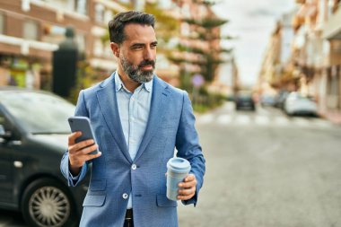Orta yaşlı işadamı akıllı telefon kullanıyor ve şehirde kahve içiyor..