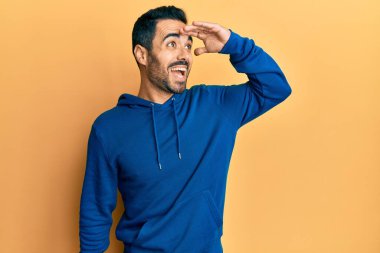 Gündelik kıyafetler giyen genç İspanyol adam çok mutlu ve gülümsüyor. Elleri başının üzerinde uzaklara bakıyor. arama kavramı. 