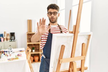 Sanat stüdyosundaki Arap genç adam avuç içleriyle jestleri durduruyor. Öfkeli ve hayal kırıklığı dolu bir ifade. 