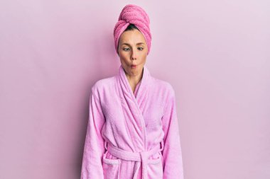 Duş başlığı ve bornoz takan genç sarışın kadın dudaklarıyla balık suratı yapıyor, çılgınca ve komik bir jest. Komik ifade. 