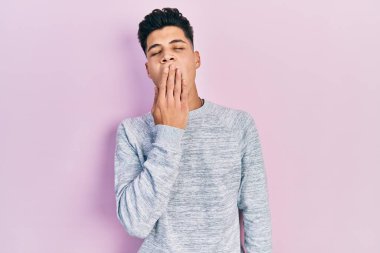 Gündelik kıyafetler giyen genç İspanyol adam ağzıyla ağzını kapatmaktan sıkılmış. Huzursuz ve uykulu.. 