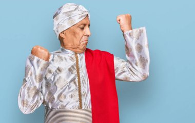 Sherwani sari giysisi giyen kıdemli İspanyol adam gururla gülümseyen kol kaslarını gösteriyor. fitness konsepti. 