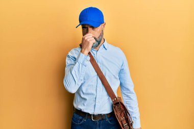 Sakallı, gri saçlı, kurye şapkalı, pis ve iğrenç bir koku alan, nefesini burnunda tutan orta yaşlı bir adam. Kötü kokuyor. 