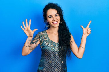 Bindi ve geleneksel kurta elbisesi giyen genç bir kadın yedi numarayı gösterip işaret ederken kendinden emin ve mutlu bir şekilde gülümsüyor.. 