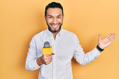 Sakallı İspanyol adam mikrofonla zaferi kutluyor mutlu bir gülümsemeyle ve ellerini kaldırarak kazanan ifadesiyle. 