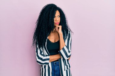 Orta yaşlı Afro-Amerikalı kadın. Elleri çenesinde gündelik kıyafetler giyip soru sormayı düşünüyor. Düşünceli bir ifade. Düşünceli bir yüzle gülümsüyor. şüphe kavramı. 