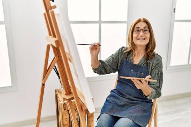 Resim stüdyosunda gülümseyen orta yaşlı bir sanatçı..