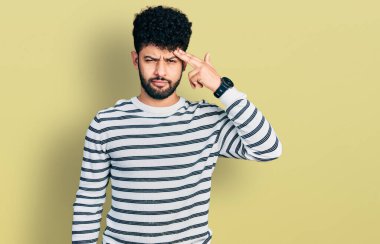 Sıradan çizgili kazak giyen sakallı genç Arap adam alnındaki sivilceden mutsuz, siyah noktalı çirkin bir enfeksiyon taşıyor. sivilce ve deri problemi 