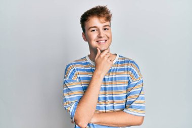 Sıradan çizgili tişört giyen genç, beyaz bir adam kameraya kollarını kavuşturup çenesine dokunarak gülümsüyor. Olumlu düşünmek. 