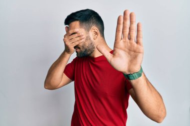 Latin kökenli genç bir adam, günlük kıyafetler giyip, elleriyle gözlerini kapatıyor ve üzgün ve korku ifadeleriyle jestleri durduruyor. utangaç ve olumsuz kavram. 